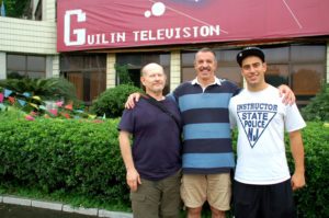 Three men pose outside the Guilin Television building