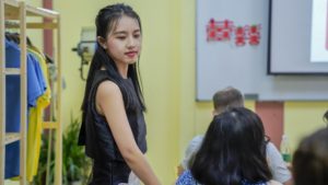 A paper-cutting instructor turns toward students seated in a classroom