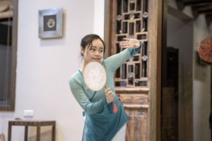 A performer in a teal dress poses with a round fan