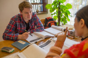A student in a plaid shirt works through a textbook with his teacher