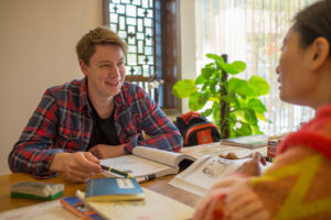 A student in a plaid shirt smiles while studying across from a teacher