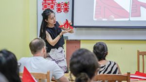 An instructor shows a red paper-cut design to a seated class