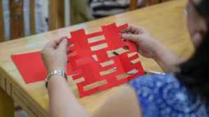 Hands hold up a red double happiness paper cutting over a table