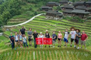 A group holds a red CLI banner on green rice terraces below a village