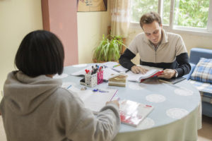 A student studies at a round table as his teacher works across from him