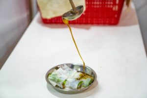 Sauce is poured from a ladle over a plated street snack
