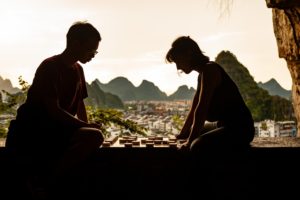 Two people play Chinese chess in silhouette above the city at sunset
