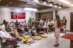 A singer performs for a seated audience in a room with a CLI sign