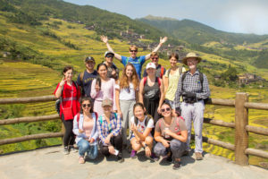 A cheerful group poses at a rice terrace viewpoint with mountains behind