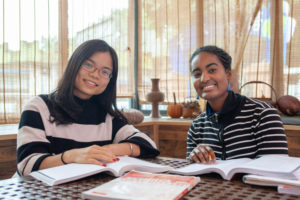A teacher and a student smile at the camera over open textbooks