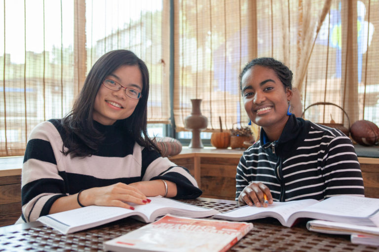 Deux étudiants souriants penchés sur leurs livres à une table de travail