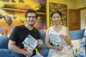 A student and teacher hold Chinese textbooks and smile on a sofa