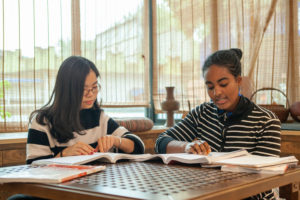 A teacher and student study open textbooks at a wooden table