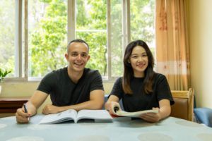 A student and teacher smile at a table with an open textbook