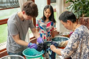 A student dips fabric into a dye bucket as an instructor helps