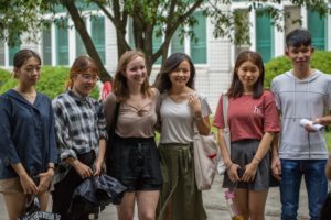 Six people stand together outside a building under trees