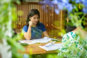 A student holds a pen to her lips while studying at a table framed by flowers