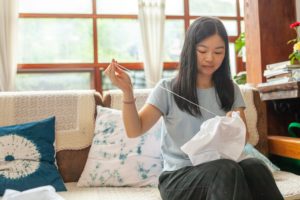 A woman on a sofa sews white fabric by hand for tie-dye