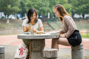 Two women play Go at a round stone table in a riverside park
