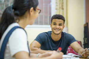 A smiling student talks with his teacher across a table