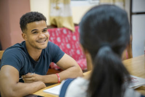A smiling student talks with a teacher across a table during a lesson