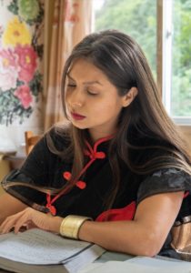 A student in a black qipao writes Chinese characters in a notebook