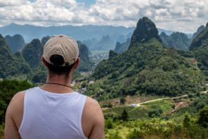 A man in a cap looks out over green karst mountains