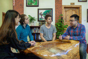 Four people sit and talk around a polished wooden table