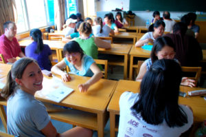 Students work together at wooden desks in a busy classroom