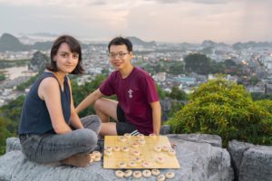 Two people sit beside a Chinese chess board on a viewpoint above the city