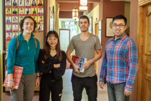 Four people with books stand together and smile in a hallway