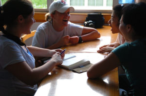 Students lean in and talk around a classroom desk by the window