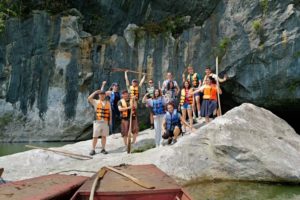 A group in life jackets poses on rocks beneath a tall limestone cliff