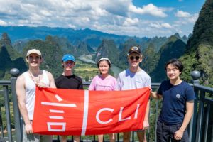Five people hold a red CLI banner at a railing above karst peaks