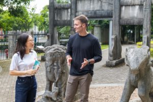 Two people talk among stone statues in a traditional Chinese garden