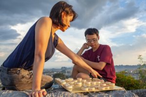 Two people play Chinese chess on a mountaintop at sunset