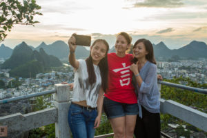 Three friends take a selfie at a mountain overlook above the city at sunset