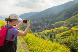 A hiker takes a phone photo of a village and rice terraces