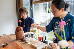 A teacher pours tea while a student watches during a tea demonstration