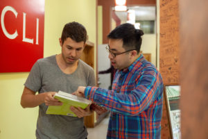 A teacher shows an open book to a student beside the red CLI sign