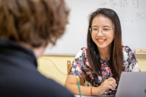 A smiling teacher works on a laptop during a one-on-one class