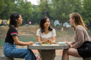 Three women smile around a stone table in a park, a Go game between them