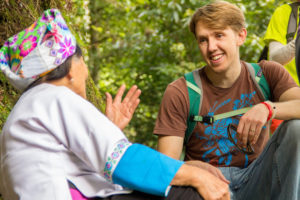 A smiling man talks with a woman in an embroidered headscarf and blue sleeves