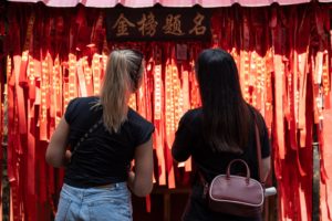Two women look at a wall of red wishing ribbons