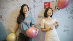 Two smiling women with balloons stand before a signed CLI wall