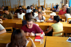 Students talk around wooden desks in a crowded classroom
