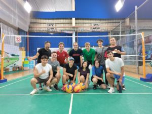 A group poses beside the net on a green indoor volleyball court