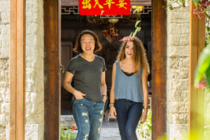 Two women walk out of a courtyard doorway under a red banner