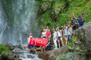 A group holds a red CLI banner on wet rocks beside a waterfall