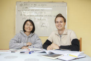 A teacher and student smile at the camera in front of a whiteboard